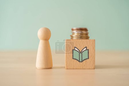 Foto de A wooden block with a book icon and coins on wooden table - Imagen libre de derechos