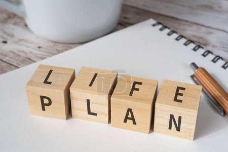 Holzblöcke mit Konzepttext "LIFE PLAN", einem Stift, einem Notizbuch und einer Tasse.