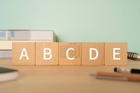 Photo for Wooden blocks with "ABCDE" text of concept, pens, notebooks, and books. - Royalty Free Image