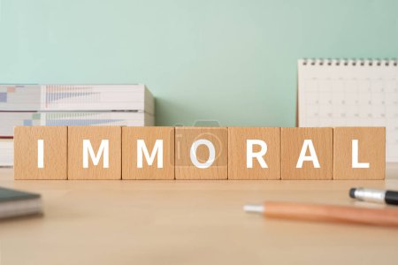 Téléchargez les photos : Wooden blocks with "IMMORAL" text of concept, pens, notebooks, and books. - en image libre de droit