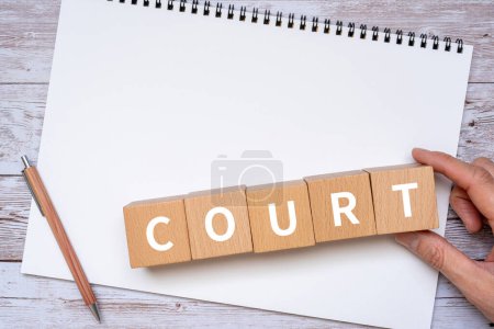 Photo for Wooden blocks with "COURT" text of concept, a pen, a notebook, and a hand. - Royalty Free Image