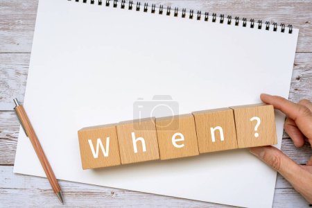 Foto de Bloques de madera con "¿Cuándo?" texto del concepto, un bolígrafo, un cuaderno y una mano. - Imagen libre de derechos