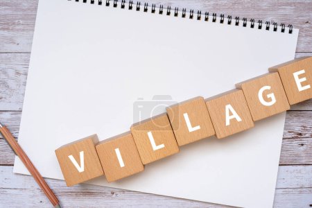 Photo for Wooden blocks with "VILLAGE" text of concept, a pen, and a notebook. - Royalty Free Image