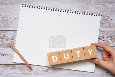 Téléchargez les photos : Main tenant des blocs en bois avec "DUTY" texte de concept, un stylo, et un carnet - en image libre de droit
