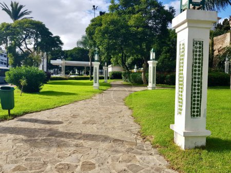 Dekorative Säulen und ein Pfad zwischen Gras und Grün im öffentlichen Park, Die verzierten Säulen stehen wie ein Wächter inmitten dieses grünen Paradieses, das Juwel im Herzen der Stadt.