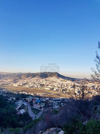 A view of the city of Tetouan, Granada's twin from above in the distance, where twin of Granada is set in the vast cityscape in the evening where shadow and sunlight meet the horizon between mountains