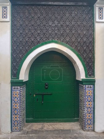 Treten Sie ein in eine Welt maurischer Eleganz, während Sie einer markanten grünen Holztür begegnen, die rundherum mit marokkanischen Zellij-Dekorationen geschmückt ist. Dieser bezaubernde Eingang verströmt den zeitlosen Charme marokkanischer Handwerkskunst, wobei das grüne Holz die 