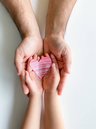 Foto de Las manos de adultos y niños sostienen un pequeño corazón de papel rojo. Día del Padre. Familia, amor, padres, hijos, cuidado, ternura - Imagen libre de derechos