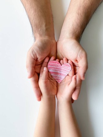 Foto de Las manos de adultos y niños sostienen un pequeño corazón de papel rojo. Día del Padre. Familia, amor, padres, hijos, cuidado, ternura - Imagen libre de derechos