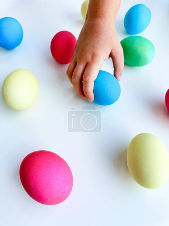Childs hand picking up a blue Easter egg among colorful eggs on a white surface, interactive and engaging holiday activity concept. Can be used for educational content highlighting fine motor skills