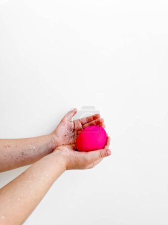 Hände, die ein rosafarbenes Ei mit Glitzern, Ostervorbereitung und festlichem Aktivitätskonzept auf weißem Hintergrund mit Kopierraum halten. Zu Ostern kreative Inhalte und Ideen für Familienaktivitäten. Hoch