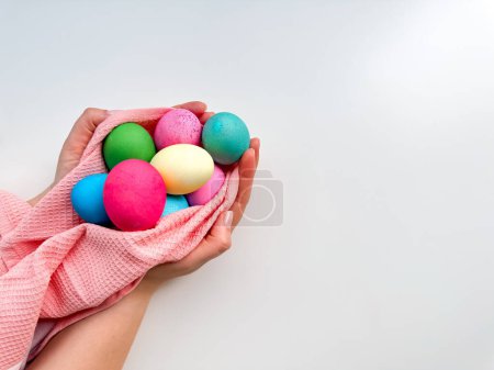 Hands tenderly hold variety of colorful Easter eggs wrapped in soft pink fabric on white background with empty space for text. Suitable for seasonal celebrations and festive spring looks. High quality