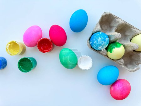 Bunt bemalte Ostereier verstreut neben offenen Dosen mit bunter Farbe und einem Eierkarton auf hellweißem Hintergrund, festliches DIY-Konzept mit Platz für Text. Hochwertiges Foto
