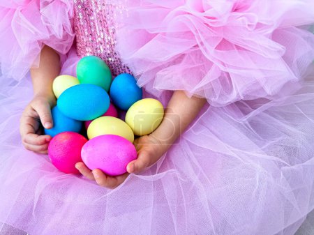 Niño en vestido de tul rosa sostiene en sus manos un puñado de brillantes huevos de Pascua multicolores, que simbolizan las vacaciones de primavera y la celebración de la Pascua. Foto de alta calidad