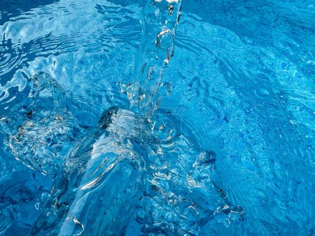 Dynamisches Spritzen in kristallklarem blauem Wasser und Glasflasche, wodurch Wellen und Wassertröpfchen in Bewegung gesetzt werden. Konzept für sauberes Wasser. Hochwertiges Foto