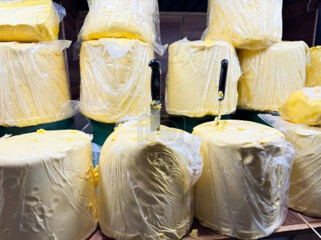 Grandes bloques de mantequilla envueltos en un paquete de plástico con cuchillos insertados, exhibidos en un estante de madera en el puesto del mercado. Industria alimentaria. Foto de alta calidad