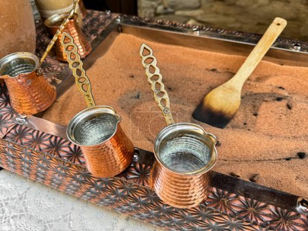 Café tradicional turco en turcos de cobre con asas largas en bandeja con arena. Preparación de café real, cierre con enfoque selectivo. Foto de alta calidad