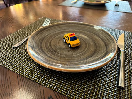 Miniature taxi toy on ceramic plate with cutlery. Concept of calling taxi after end of banquet or celebration. Design of taxi advertising, culinary presentations and unusual concepts. High quality