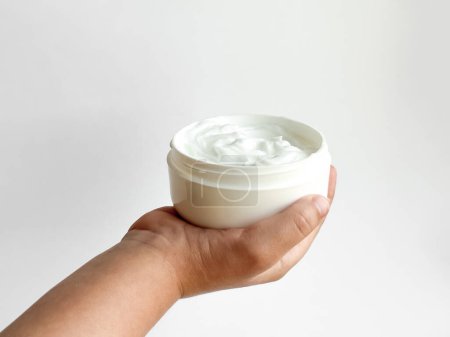 Close up of childs hand holding container of cream on white background with copy space. Skincare and moisturizing concept. Design for healthcare, wellness, and child care poster. High quality photo