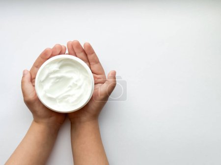 Close up of childs hands holding container of hand cream on white background with copy space. Skincare and moisturizing concept. Design for healthcare and wellness. High quality photo