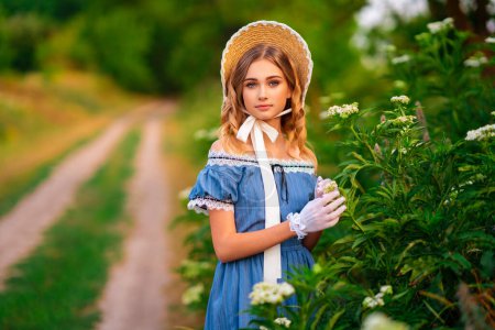 Schöne junge Mädchen in Vintage-blaues Kleid und Strohhut hält eine Blume im Feld auf grünem Hintergrund. Prinzessin auf Natur.