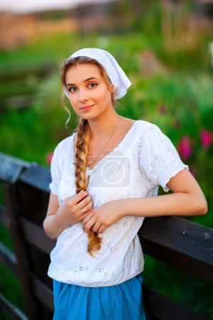 Téléchargez les photos : Portrait de Belle fille blonde aux cheveux tressés en vêtements ruraux blancs. Vie à la ferme.Jeune mannequin posant sur un ranch.. - en image libre de droit