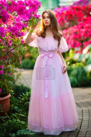 Belle fille en robe vintage rose et chapeau de paille debout près de fleurs colorées. Oeuvre d'art de femme romantique. Jolie modèle de tendresse posant et regardant la caméra.