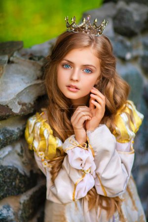 Photo for Beautiful young blonde princess in gold medieval dress and little crown. Pretty queen posing near stone castle.Warm art work. - Royalty Free Image