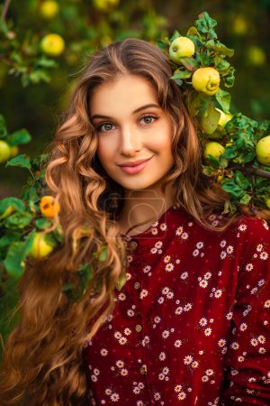 Photo for Portrait of a curly long hair Beautiful girl in a red velvet dress and shawl posing in apple garden. Art work of romantic woman .Pretty tenderness model looking at camera. - Royalty Free Image