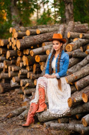 Photo for Beautiful cowgirl with extra long braided hair in vintage lace dress and orange hat posing on ranch . Portrait of a pretty model in countryside. Warm art. - Royalty Free Image