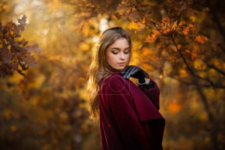 Téléchargez les photos : Gros plan portrait d'une belle fille en robe sombre debout près de feuilles d'automne colorées. Oeuvre d'art de femme romantique. Jolie modèle de tendresse regardant vers le bas. - en image libre de droit