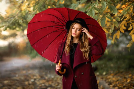 Téléchargez les photos : Gros plan portrait d'une belle fille en robe sombre et chapeau noir debout près de feuilles d'automne colorées avec parapluie. Oeuvre d'art de femme romantique. Jolie modèle de tendresse regardant vers le bas. - en image libre de droit