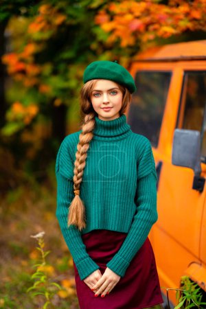 Photo for Portrait of young beautiful blonde girl with blue eyes and braided hair.Attractive model in green knitted sweater and beret standing near old retro orange bus with autumn background. Colorfull art. - Royalty Free Image