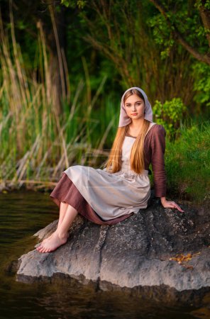 Photo for Pretty young laundress in medieval costume standing near river. Fairytale art work. - Royalty Free Image