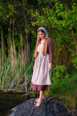 Photo for Pretty young laundress in medieval costume standing near river. Fairytale art work. - Royalty Free Image