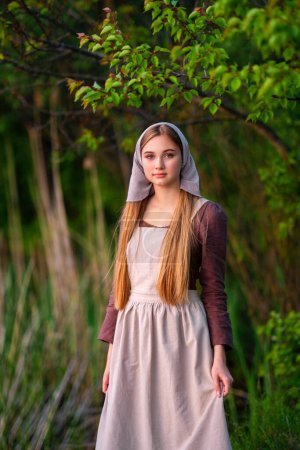 Pretty young laundress in medieval costume standing near river. Fairytale art work.