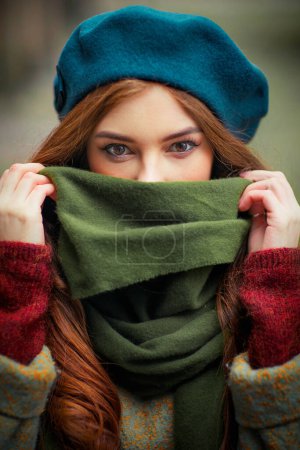 Photo for Portrait of a redhead  beautiful girl in a green scarf and blue hat standing on colorful background. Art work of romantic woman in autumn .Pretty tenderness model looking at camera. - Royalty Free Image