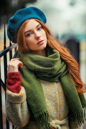 Téléchargez les photos : Portrait d'une rousse belle fille dans une écharpe verte et chapeau bleu debout sur fond coloré. Oeuvre d'art de la femme romantique en automne.Jolie modèle de tendresse regardant la caméra. - en image libre de droit