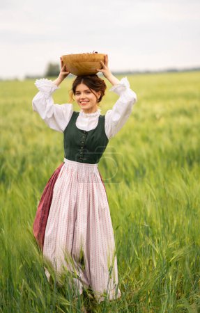 Hermosa chica pelirroja en vestido medieval de pie en un campo de trigo con cerezas. Cuento de hadas historia sobre la ternura mujer linda .Warm trabajo de arte.