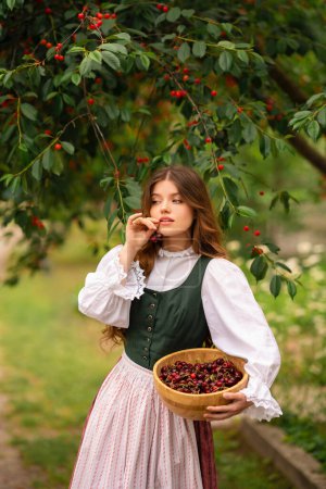 Photo for Beautiful red haired girl in  medieval dress standing near cherry tree . Fairy tale story about tenderness cute woman .Warm art work. - Royalty Free Image