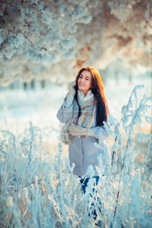 Photo for Portrait  of beautiful brunette girl in warm scarf outdoor in winter frost forest .Pretty young model on blue background smiling. - Royalty Free Image