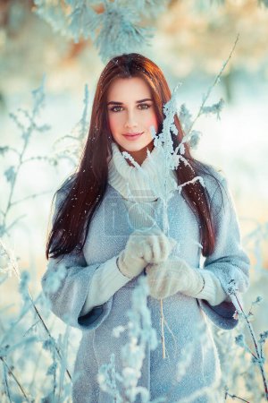 Photo for Portrait  of beautiful brunette girl in warm scarf outdoor in winter frost forest .Pretty young model on blue background smiling. - Royalty Free Image