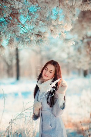Téléchargez les photos : Portrait de belle fille brune en écharpe chaude en plein air dans la forêt de gel d'hiver.Jolie jeune modèle sur fond bleu souriant. - en image libre de droit