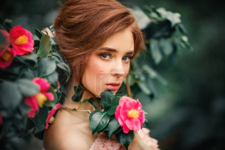 Téléchargez les photos : Gros plan portrait d'une belle fille aux cheveux roux dans une robe vintage rose debout près de fleurs colorées. Oeuvre d'art de femme romantique. Jolie modèle de tendresse regardant la caméra. - en image libre de droit