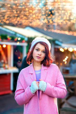 Photo for Portrait of a beautiful young model in a knitting cap standing on a christmas background with bokeh lights. Magic warm new year photo.Cozy background of winter fair. Happy woman. - Royalty Free Image