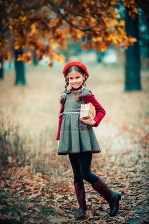 Téléchargez les photos : Portrait d'automne d'une belle jeune écolière en béret rouge et poils tressés avec livres. Sensibilité enfant positif avec sourire lumineux profiter de la nature dans le parc. - en image libre de droit