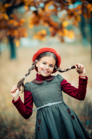 Photo for Autumn portrait of a beautiful young schoolgirl in red beret and braid hairs. Tenderness positive child with bright smile enjoying nature in park. - Royalty Free Image