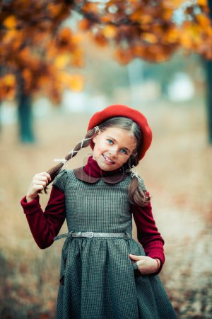 Photo for Autumn portrait of a beautiful young schoolgirl in red beret and braid hairs . Tenderness positive child with bright smile enjoying nature in park. - Royalty Free Image