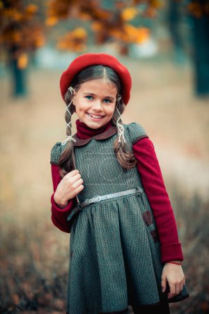 Photo for Autumn portrait of a beautiful young schoolgirl in red beret and braid hairs . Tenderness positive child with bright smile enjoying nature in park. - Royalty Free Image