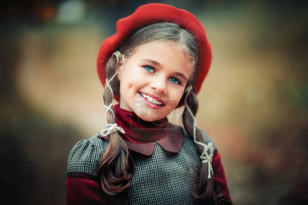 Photo for Autumn portrait of a beautiful young schoolgirl in red beret and braid hairs  . Tenderness positive child with bright smile enjoying nature in park. - Royalty Free Image